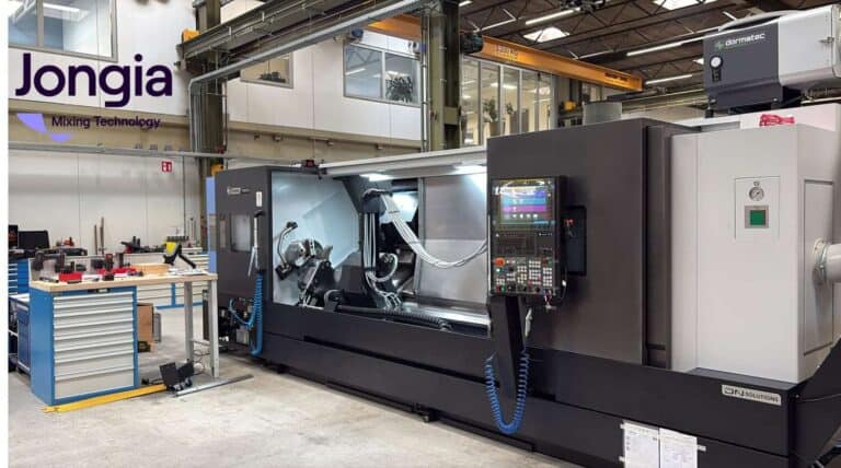 Een grote CNC-machine staat in een industriële werkplaats met gereedschap en apparatuur in de buurt. De machine heeft een digitaal bedieningspaneel en het logo van Jongia Mixing Technology is zichtbaar aan de muur. Op de achtergrond zijn kranen en planken te horen.