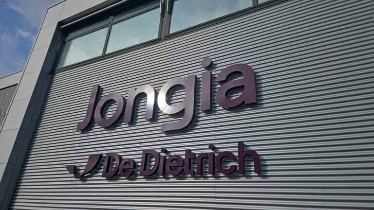 Een gevel van gegolfd metalen gebouw met grote, donkerpaarse 3D-letters die "Jongia" spellen boven een kleiner "De Dietrich"-logo en tekst. Het gebouw heeft grote ramen boven het bord en een blauwe lucht is zichtbaar in de linkerbovenhoek.