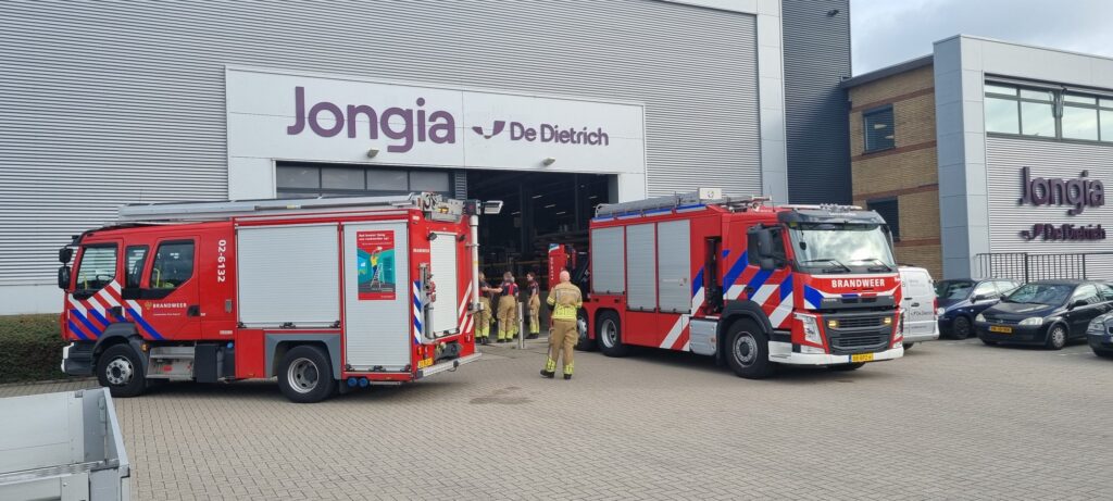 Two fire engines parked outside the Jongia De Dietrich building during Safety Day, with firefighters walking into the production hall.