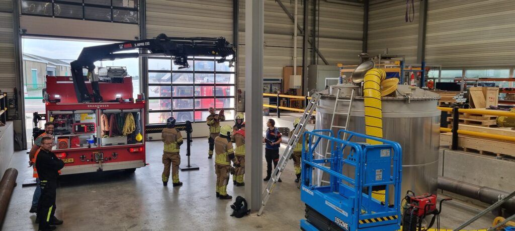 Firefighters and Jongia colleagues next to the storage tank and fire engine in the production hall during the rescue demonstration.