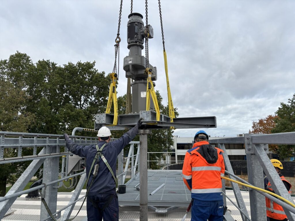 Engineers guide the drive and mounting frame of the Jongia agitator out of the bridge opening on the sludge mixing tank.
